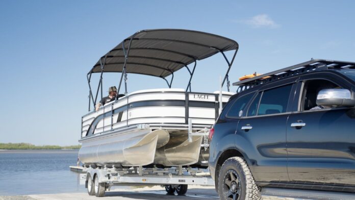 Car reversing pontoon boat on trailer for beach launch while boating in Queensland